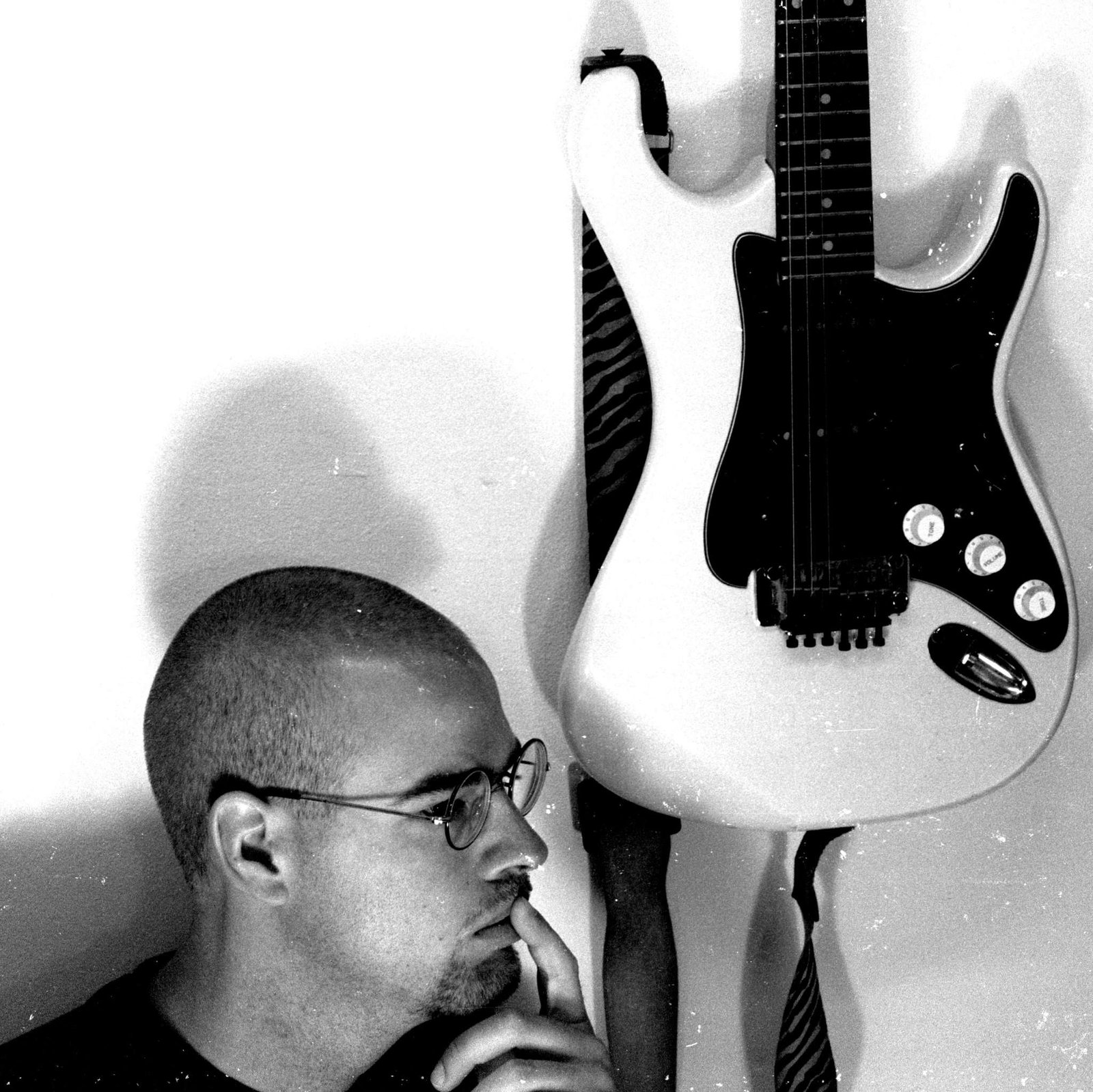 Matthew B. Hembree Black & White Portrait with Guitar Black and white portrait of Matthew B. Hembree in deep thought next to a white electric guitar hanging on the wall.